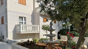 Une cour agrémentée d’une fontaine, d’une statue et de diverses plantes et fleurs.