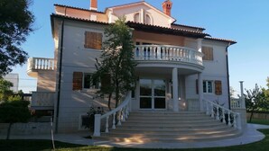 Une maison à deux étages avec un balcon, un escalier d’entrée et un jardin.
