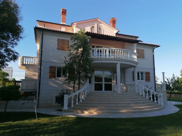 Une maison à deux étages avec un balcon, un escalier d’entrée et un jardin.
