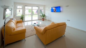 Un salon avec deux canapés jaunes, une table basse en verre, un téléviseur fixé au mur et une plante en pot.