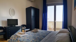Ett hotellrum med en säng, en tv på en byrå, en garderob och en balkong med blå gardiner.