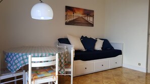 A room with a bunk bed, a small table with a patterned tablecloth, and a painting of a pier on the wall.