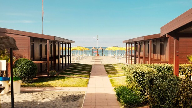 Ett hotell vid stranden med träkonstruktioner, en sandpromenad och gula parasoller.