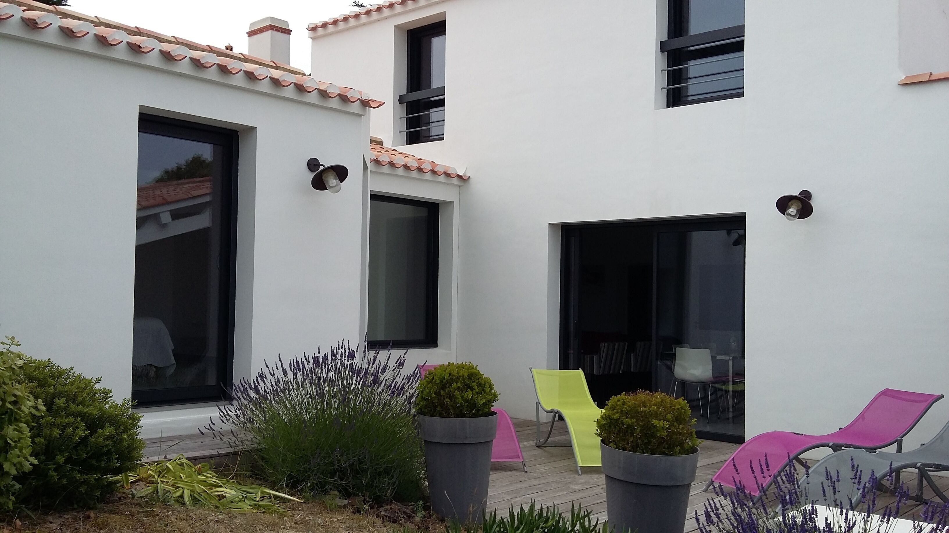 A modern building with white exterior walls, large windows, and a patio area with potted plants and outdoor furniture.