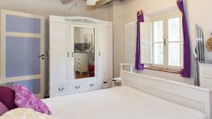Un dormitorio con cama, armario, ventana con cortinas y radiador.
