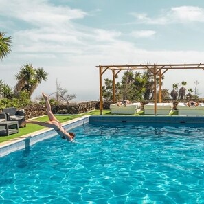 Ein Schwimmbecken mit einer Person, die ins Wasser springt, Liegestühlen und einer Pergola.