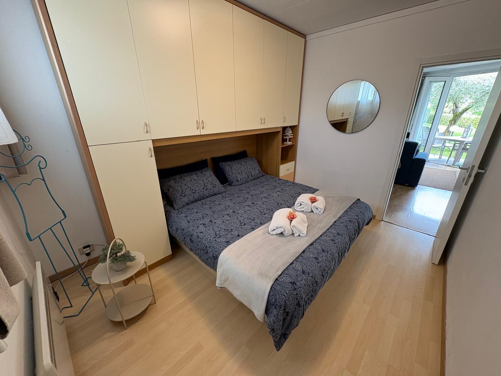 Ein Schlafzimmer mit Bett, Kleiderschrank, runder Spiegel und einem kleinen Tisch mit Pflanze.