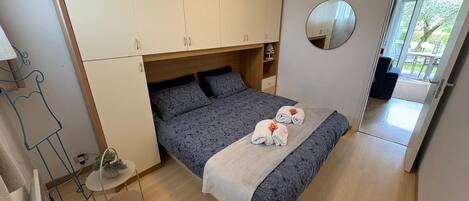Ein Schlafzimmer mit Bett, Kleiderschrank, runder Spiegel und einem kleinen Tisch mit Pflanze.