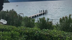 A lakeside view with a wooden pier extending into the water, surrounded by lush greenery and a mountainous backdrop. - Direct Lake Access: Panoramic Pool, Jetty & Parking (manerba del garda)