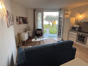 Un espacio habitable compacto con sofá, mesa de comedor, área de cocina y puerta corrediza de vidrio que da a un jardín.