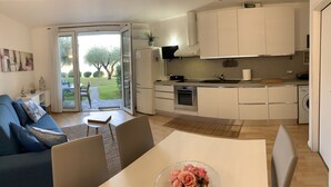 A modern kitchen with white cabinets, a built-in oven, and a sink. There's a dining area with a table and chairs, and a sofa with cushions. - Direct Lake Access: Panoramic Pool, Jetty & Parking (manerba del garda)