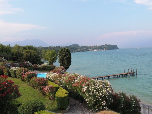 A landscaped garden with a swimming pool, a wooden dock extending into a lake, and a distant view of a mountainous landscape.