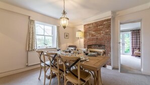 A dining area with a brick fireplace, wooden chairs, and a table set for four. - Tusker House, Wells-next-the-Sea, Norfolk (Wells-next-the-Sea)