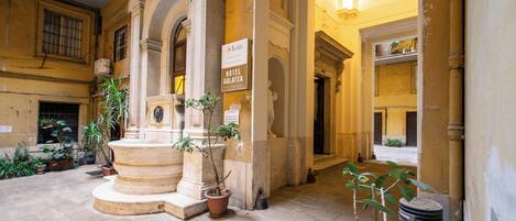 Une cour avec une fontaine, des plantes en pot et une enseigne indiquant l’hôtel Galatea.