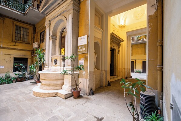 A courtyard with a fountain, potted plants, and a sign for the Hotel Galatea.