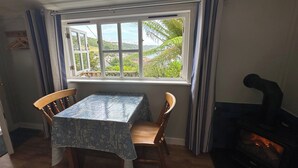 A dining area with a table and chairs, a window with curtains, and a fireplace. - The Crow's Nest - A Cosy Village Cottage with Stunning Sea Views (Cawsand)