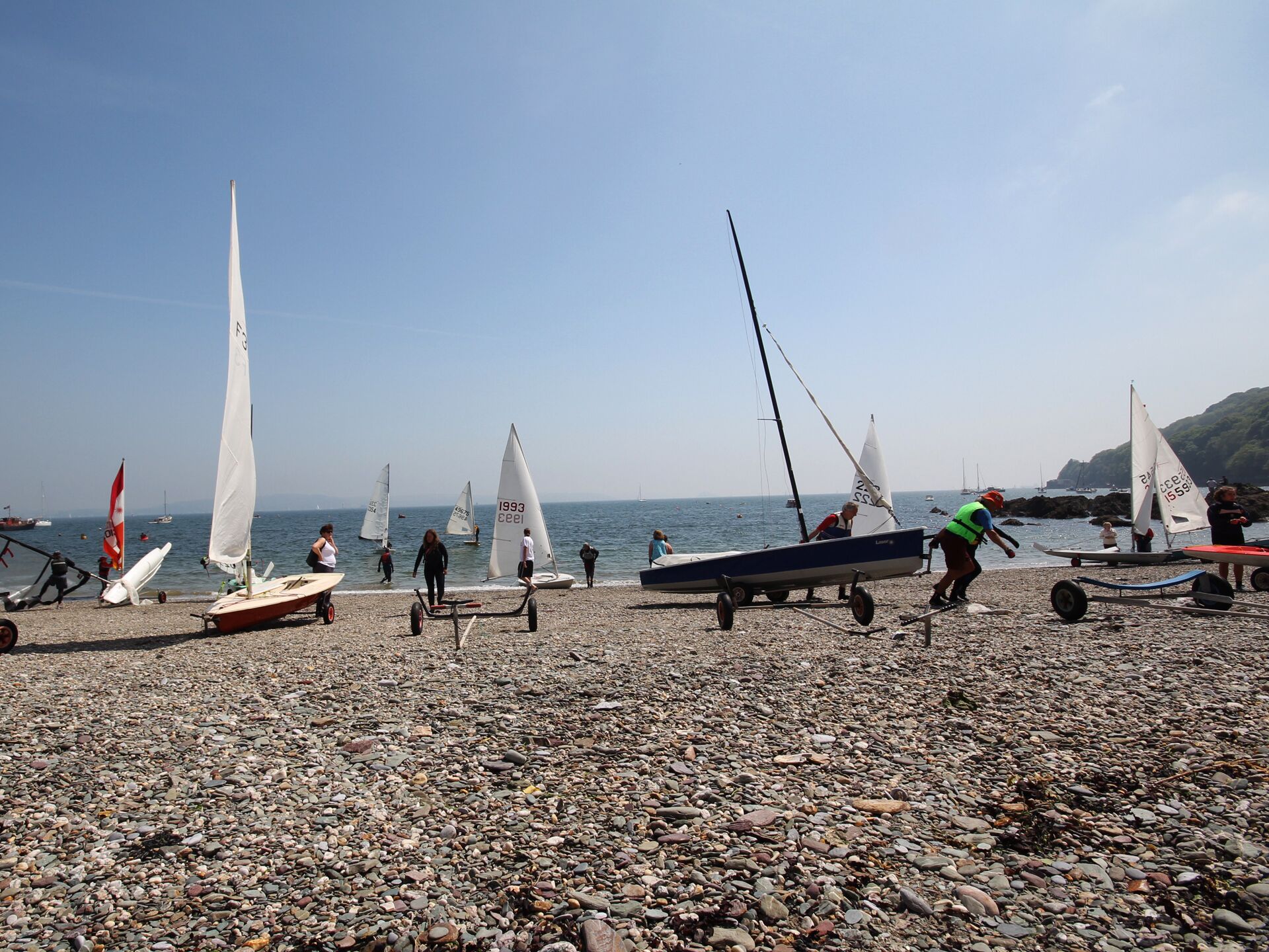 A pebbled beach with sailboats and people.