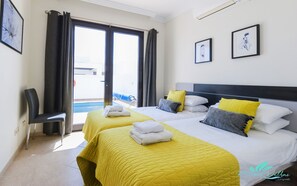 A hotel room with two beds, a view of the pool, and two framed artworks on the wall.
