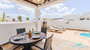 En takterrass med ett matbord för fyra personer, solstolar, en pool och en grill.