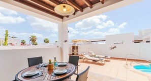 Una terraza en la azotea con una mesa de comedor para cuatro, sillones de descanso, una piscina y una parrilla.