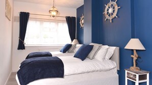 Une chambre avec deux lits, une fenêtre avec des rideaux, une décoration représentant un gouvernail de bateau et une lampe sur une table de chevet.