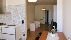 A modern kitchen with a gas stove, white cabinets, and a tiled backsplash. There is a dining area with a wooden table and chairs, and a green chair in the background. - Penthouse on two levels at 20 meters from the sea in the center of Loano (Loano)