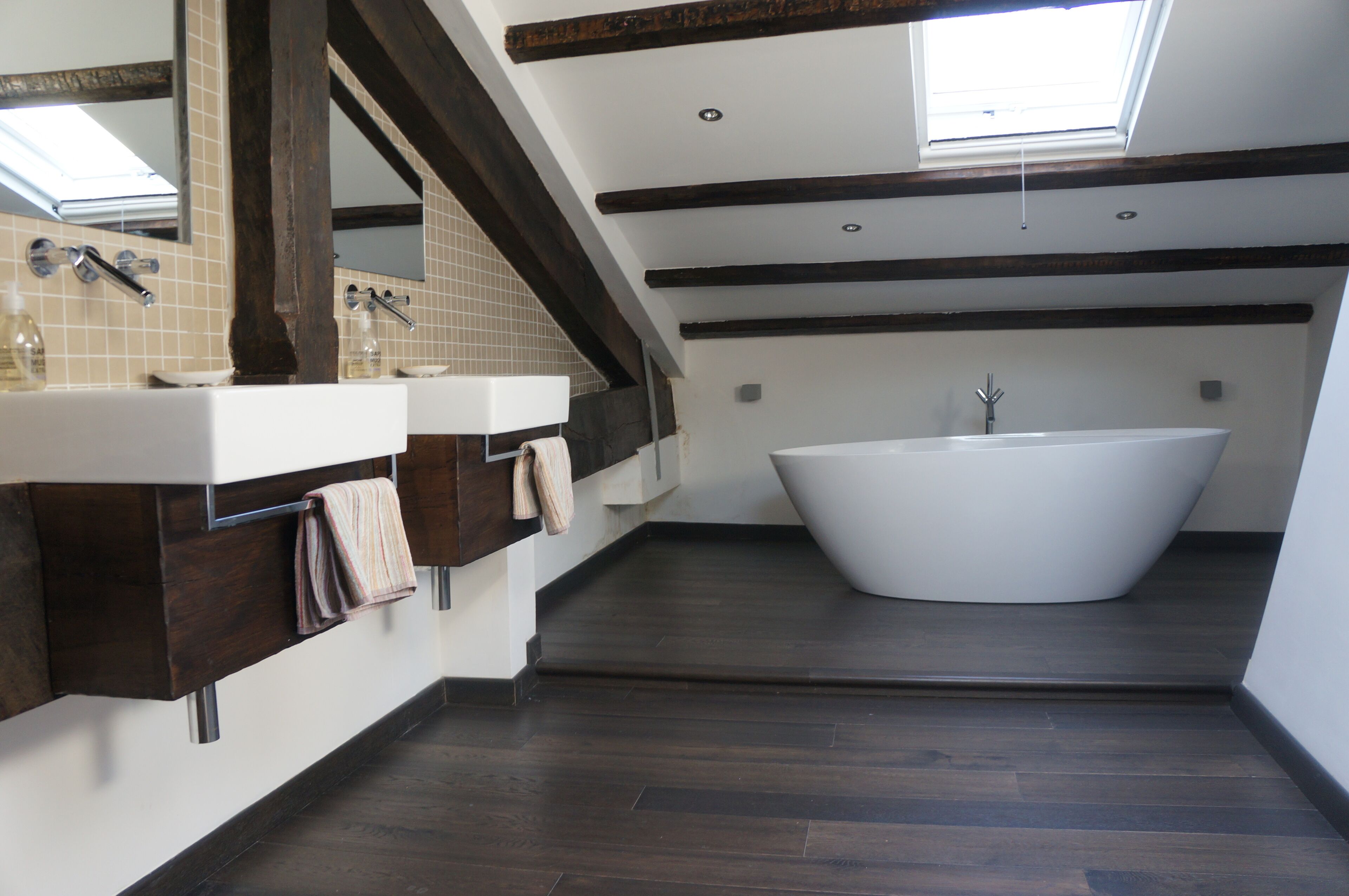 A modern bathroom with a freestanding bathtub, two sinks, and a skylight.