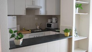 Een keuken met witte kastjes, een zwart aanrecht, een magnetron, een koffiezetapparaat en potplanten.