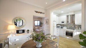 A modern kitchen with white cabinets, a microwave, and an oven. There is a dining area with a wooden table and chairs, and a vase with flowers. - Modern villa on the beach, large private pool, BBQ, many flowers very quiet. (Almuñécar)
