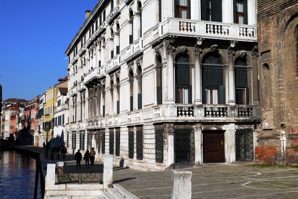 Un edificio histórico con arquitectura ornamentada, un canal y una pasarela peatonal.