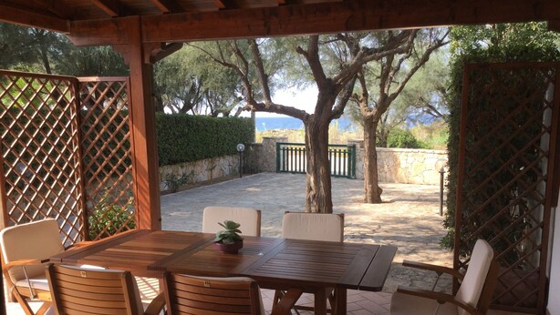 Un patio al aire libre con una mesa y sillas de madera, rodeado por una pérgola de madera.