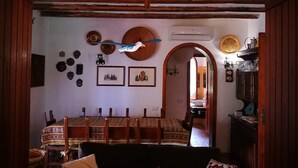 A cozy living room with a wooden ceiling, a dining area with a patterned tablecloth, and a kitchen visible through an archway. - Villa - Eden Rock - Santa Margherita di Pula - House with garden (Domus de Maria)