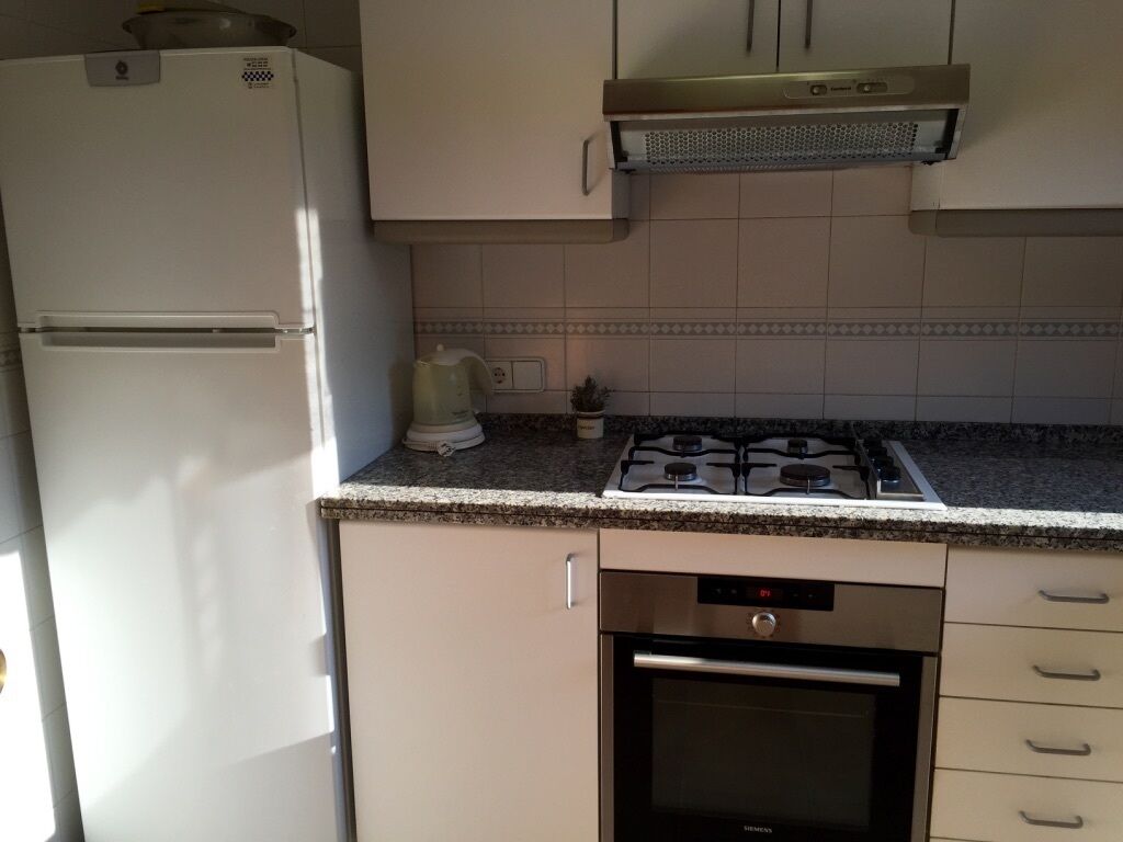 Una cocina compacta con un refrigerador blanco, una estufa a gas y un horno empotrado.