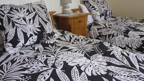 Ein Schlafzimmer mit einem Bett, das mit schwarz-weißer Blumenwäsche bezogen ist, einem Nachttisch aus Holz mit einer Lampe und einem weißen Kopfkissen.