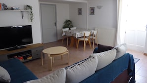 Ein Wohnzimmer mit Flachbildfernseher, einer Couch, einem kleinen runden Tisch und einem Esstisch mit Stühlen.