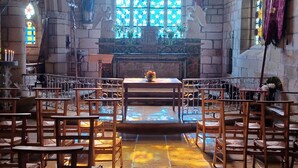 Ein Innenraum einer Kirche mit einer hohen Gewölbedecke, einem großen Buntglasfenster und Reihen hölzerner Kirchenbänke.