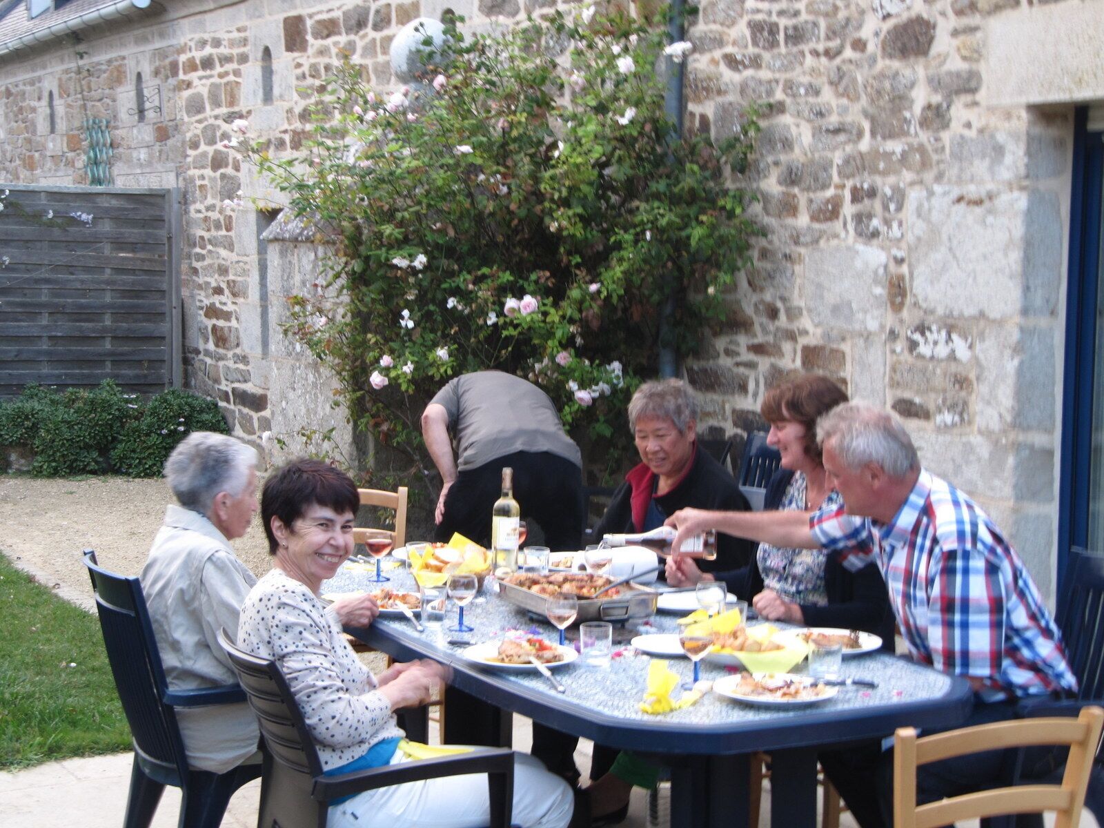 Un gruppo di persone cena all'aperto attorno a un tavolo rotondo, con cibo e bevande.