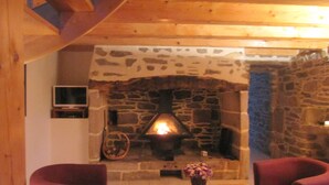 Ein gemütliches Zimmer mit Kamin aus Stein, Holzbalkendecke und Fernseher an der Wand.