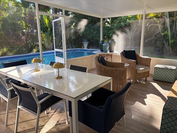 Een zonnig terras met een zwembad, rieten meubels en een tafel met lampen.