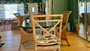 Un comedor con una mesa de vidrio rodeada de sillas de mimbre, una puerta verde y una ventana con persianas.