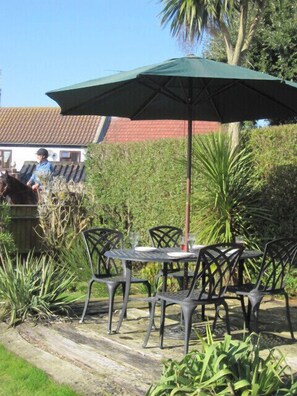 An outdoor patio with a table and chairs, a green umbrella, and a person riding a horse in the background. - Henry's Cottage - a place to make you smile (Winterton on sea)