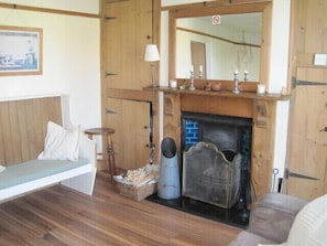 A cozy room with a wooden floor, a bench, a fireplace, and a mirror above it. - Henry's Cottage - a place to make you smile (Winterton on sea)