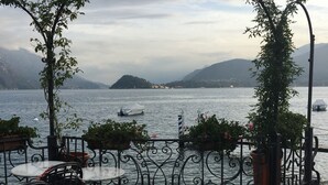 Een café aan het water met terras, uitzicht op het meer en bergen op de achtergrond.