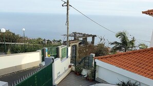 A silver car parked in a narrow driveway with a green gate, a tiled patio area, and a view of the sea. - Panoramic view over the city and the sea (Funchal)