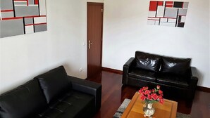 A living room with a black leather sofa, a wooden coffee table with a vase of red flowers, and abstract wall art. - Panoramic view over the city and the sea (Funchal)