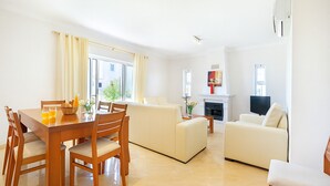 Een moderne woonkamer met een eethoek, voorzien van een open haard, een flatscreen-televisie en een groot raam met gordijnen.