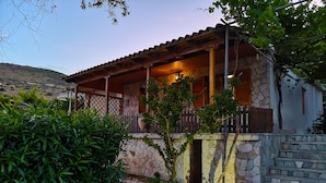 A stone house with a wooden porch and a stone staircase leading to the entrance. - Shipwreck - Navagio house (Zakinthos)