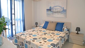 Une chambre à coucher comprenant un lit, des tables de chevet, une lampe, des rideaux, un tableau décoratif et un vase avec des fleurs.