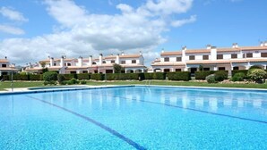 Una piscina circondata da una fila di edifici bianchi con tetti in tegole rosse, sotto un cielo azzurro limpido.