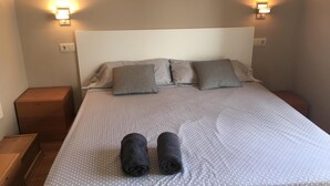 Un letto rifatto con una coperta a pois, due cuscini e due asciugamani arrotolati. Sono presenti due comodini e luci fissate al muro.